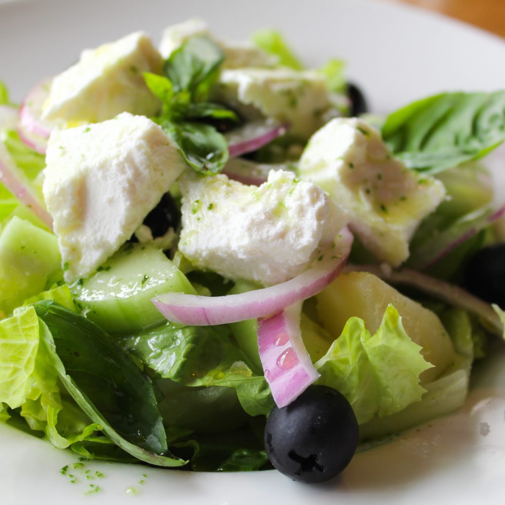 Ensalada de patata, lechuga, tomate seco, pepino, cebolla, aceitunas y queso de cabra con aliño de albahaca