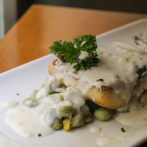 Corvina sobre lecho de habitas y cebolleta con salsa de cítricos